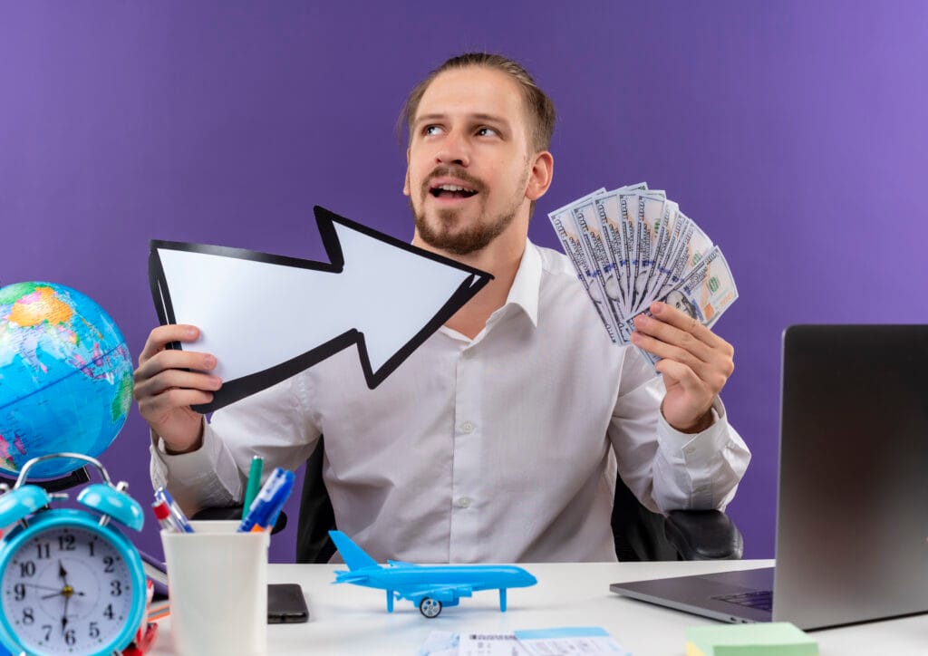 How Much Does It Cost to Hire Infix Digital? 1 handsome businessman white shirt holding white arrow showing cash looking aside with smile face sitting table offise purple background